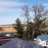 An elevated view of a parking lot and a street with trees, a house, and vehicles under a bright, partly cloudy sky.