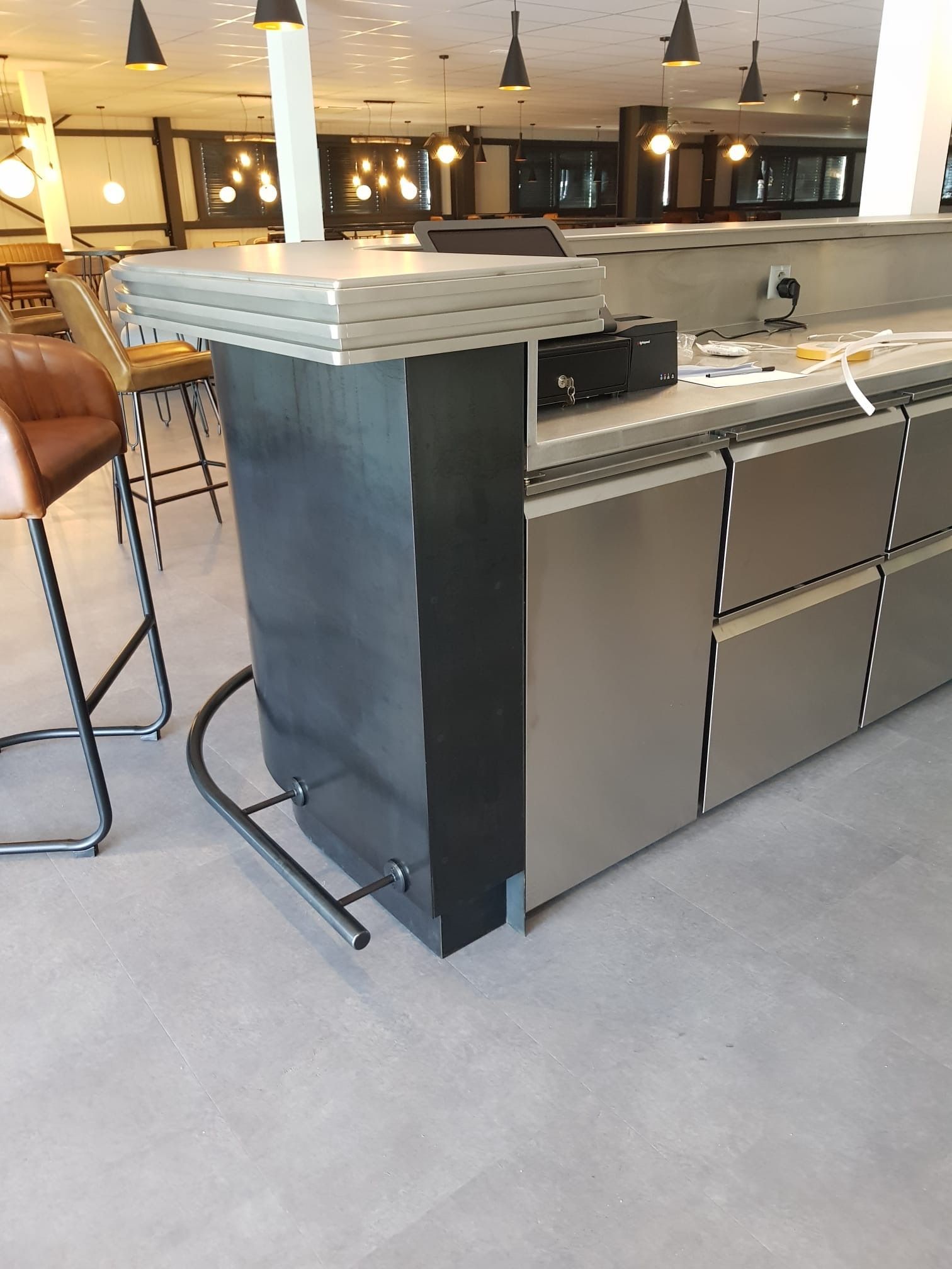 Un bar en métal avec des armoires en acier inoxydable, des tabourets de bar et un éclairage au plafond.