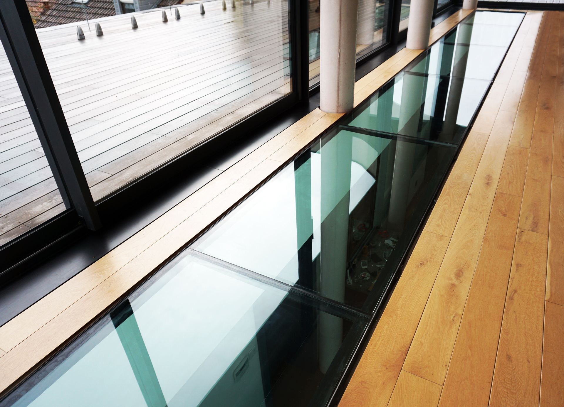 Panneaux de sol en verre adjacents à une fenêtre avec plancher en bois, laissant passer la lumière.