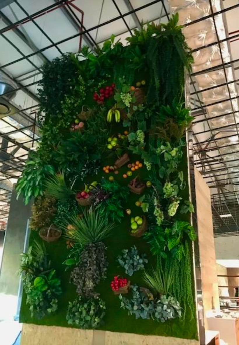 Mur de jardin vertical avec feuillage vert luxuriant, baies rouges et petits paniers suspendus, à l'intérieur.