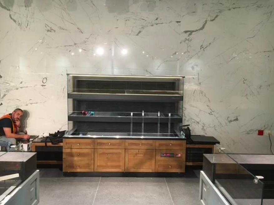 Un homme est assis près d'un comptoir d'exposition de nourriture dans un magasin aux murs en marbre ; des étagères vides.