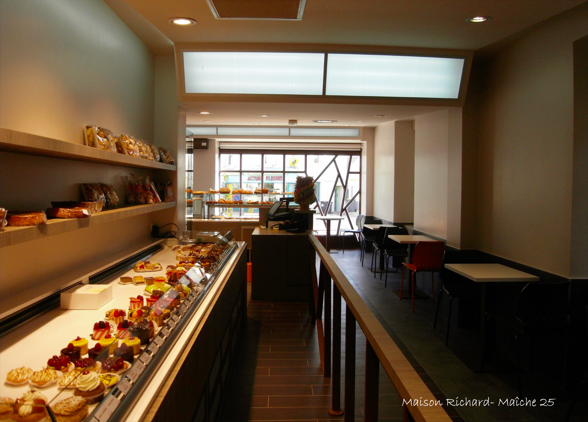Intérieur de pâtisserie avec pâtisseries exposées, petit coin salon et porte ouverte vers l'extérieur.