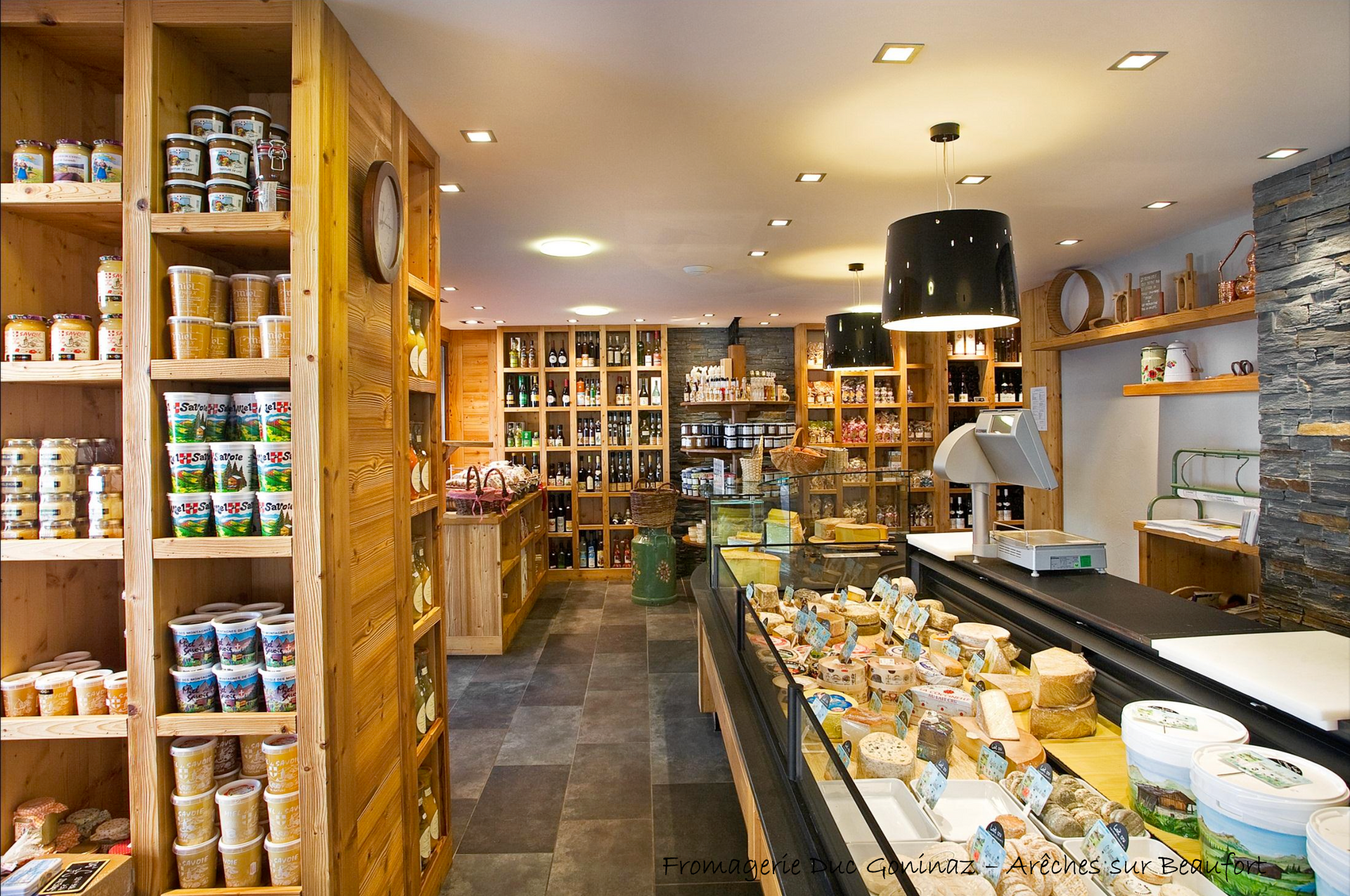 Intérieur de fromagerie avec étagères en bois et vitrine remplie de fromage.
