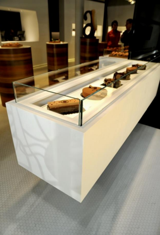 Une vitrine blanche avec plateau en verre présente des poteries dans une galerie lumineuse.