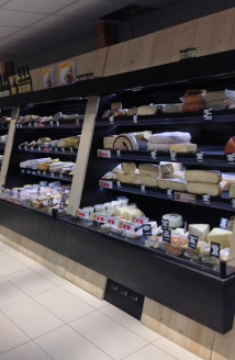 Vitrine de fromages dans une épicerie, avec différents fromages étiquetés et empilés.
