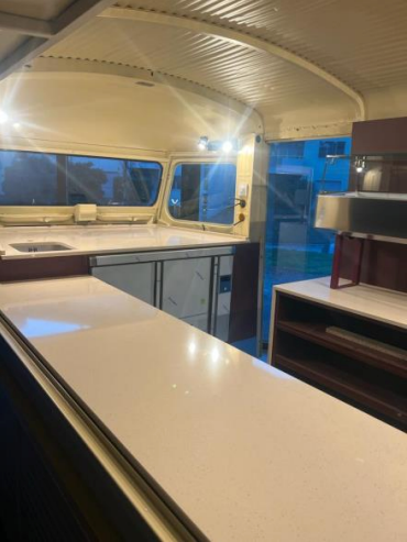 Intérieur d'un food truck avec un comptoir blanc, des armoires et un petit coin cuisine.