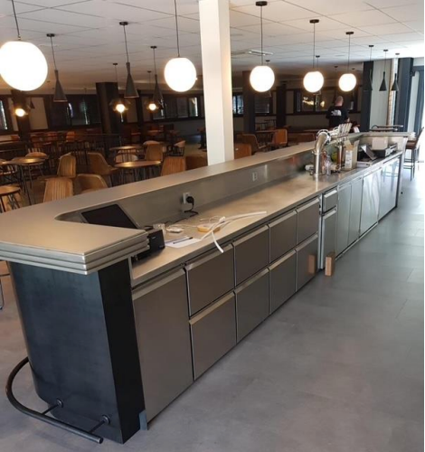 Bar de restaurant avec comptoirs en acier inoxydable, tiroirs et plafonniers.