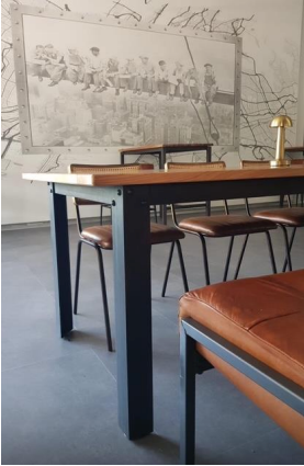 Une table à manger avec un plateau en bois et des pieds noirs, entourée de chaises en cuir marron et d'un banc.