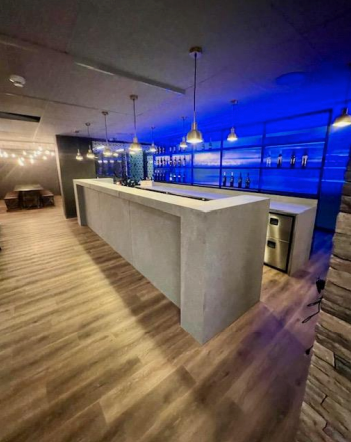 Bar avec comptoir en béton, étagères rétroéclairées bleues, luminaires suspendus, plancher en bois.