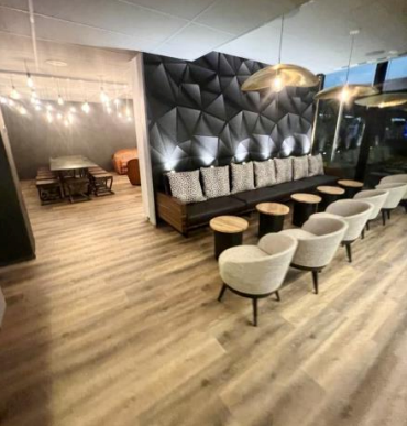 Intérieur de café moderne : mur noir géométrique, banc rembourré, petites tables, chaises de couleur claire, parquet.
