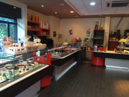 À l'intérieur d'une pâtisserie, vitrines remplies de confiseries et de viennoiseries. Parquet foncé, touches de rouge.