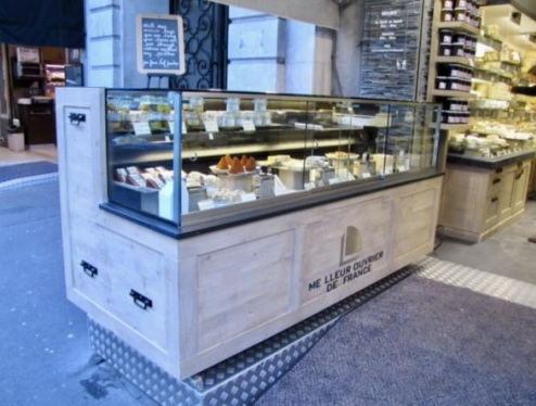 Vitrine à fromages à l'extérieur d'un magasin ; bois clair et verre, avec divers fromages.