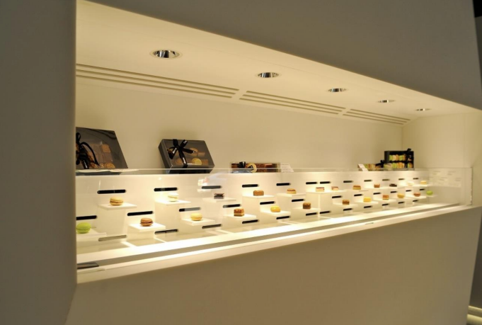 Vitrine avec petits produits alimentaires sur socles blancs, sous un éclairage lumineux.