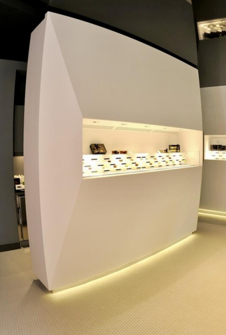 Vitrine blanche avec étagères éclairées présentant des lunettes.