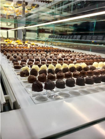 Des rangées de chocolats assortis exposés dans une vitrine en verre bien éclairée dans une chocolaterie.