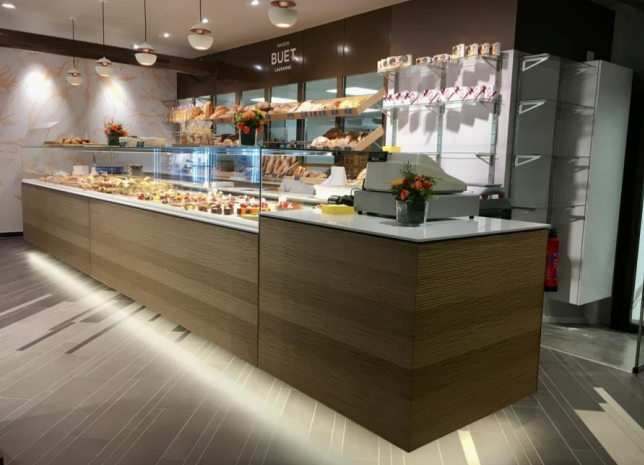 Vitrine de boulangerie remplie de viennoiseries. Comptoir en bois, plateau en marbre blanc et viennoiseries.