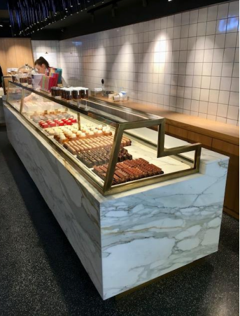 Vitrine de pâtisserie en marbre remplie de desserts colorés ; personne derrière le comptoir.