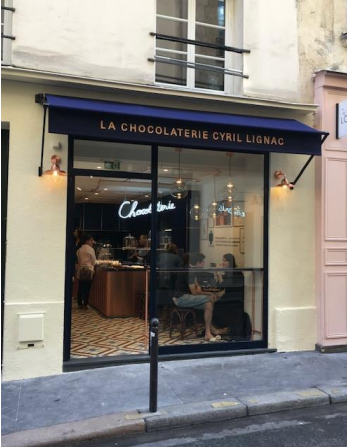 La devanture de la Chocolaterie Cyril Lignac avec un auvent bleu, des vitrines et une enseigne au néon, Paris.