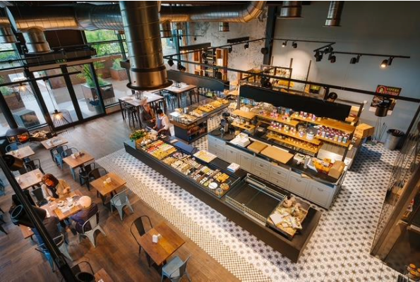 Vue aérienne d'un café avec tables, présentoirs et clients. Bois clair et carrelage à motifs.