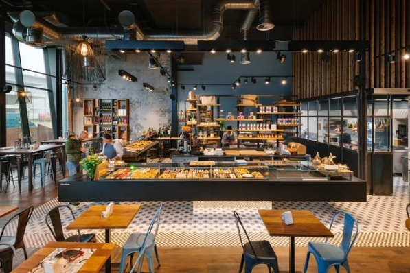 Intérieur de café avec tables en bois, chaises et une vitrine remplie de pâtisseries.