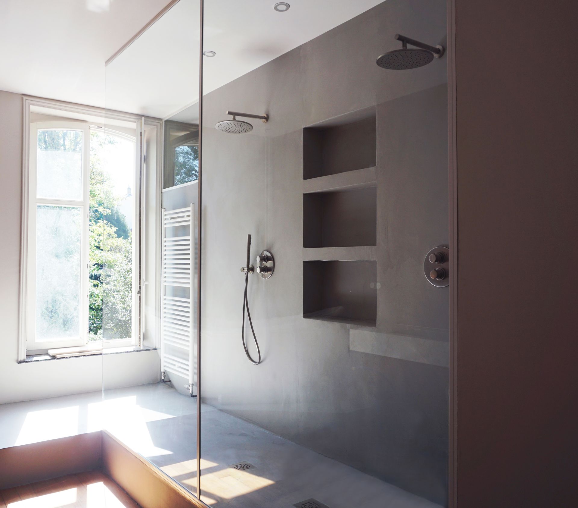 Salle de bain moderne avec douche à l'italienne, étagères et lumière naturelle provenant d'une fenêtre.