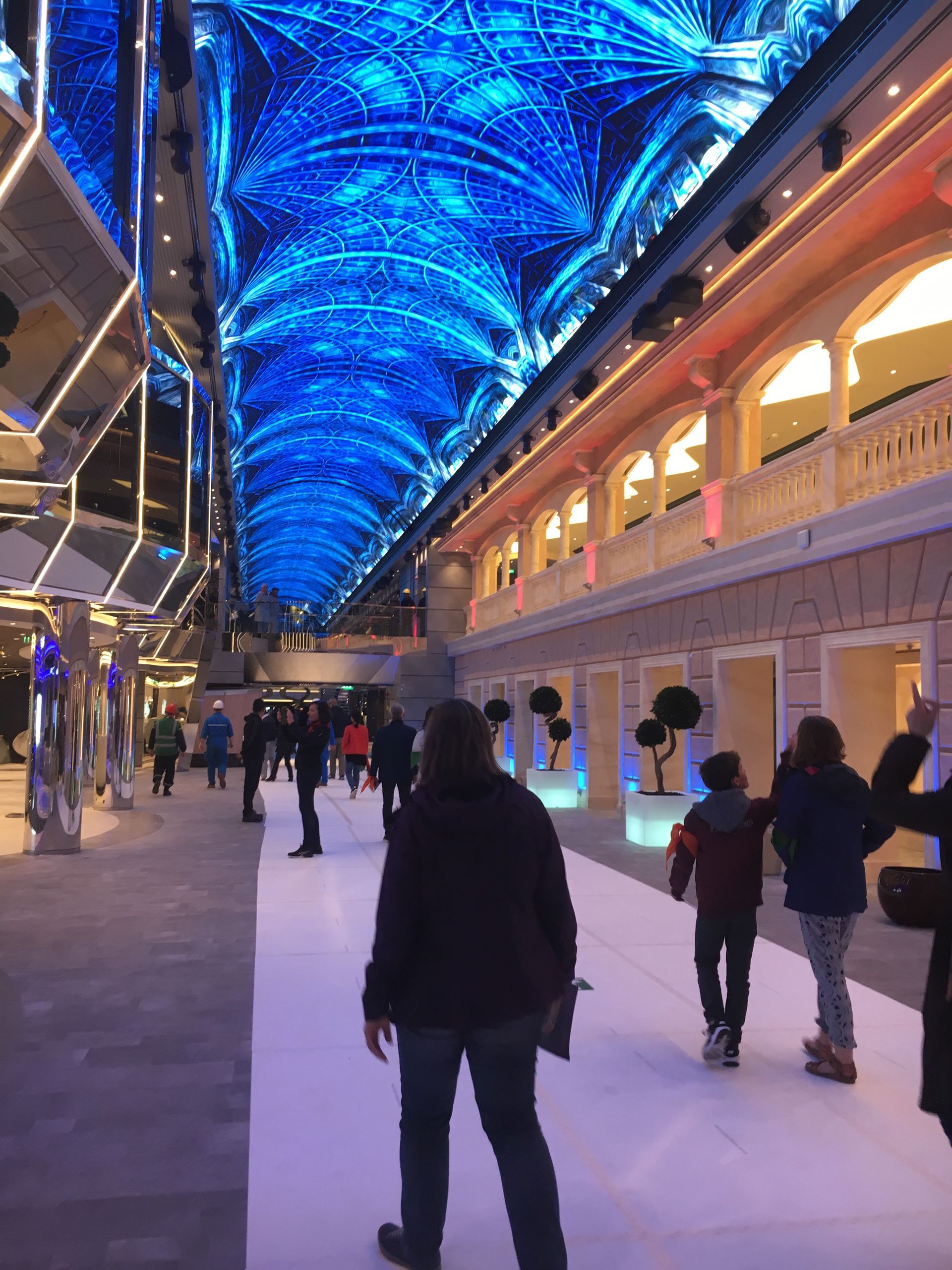 Les gens marchent sous un plafond bleu illuminé dans l'atrium d'un bateau de croisière.