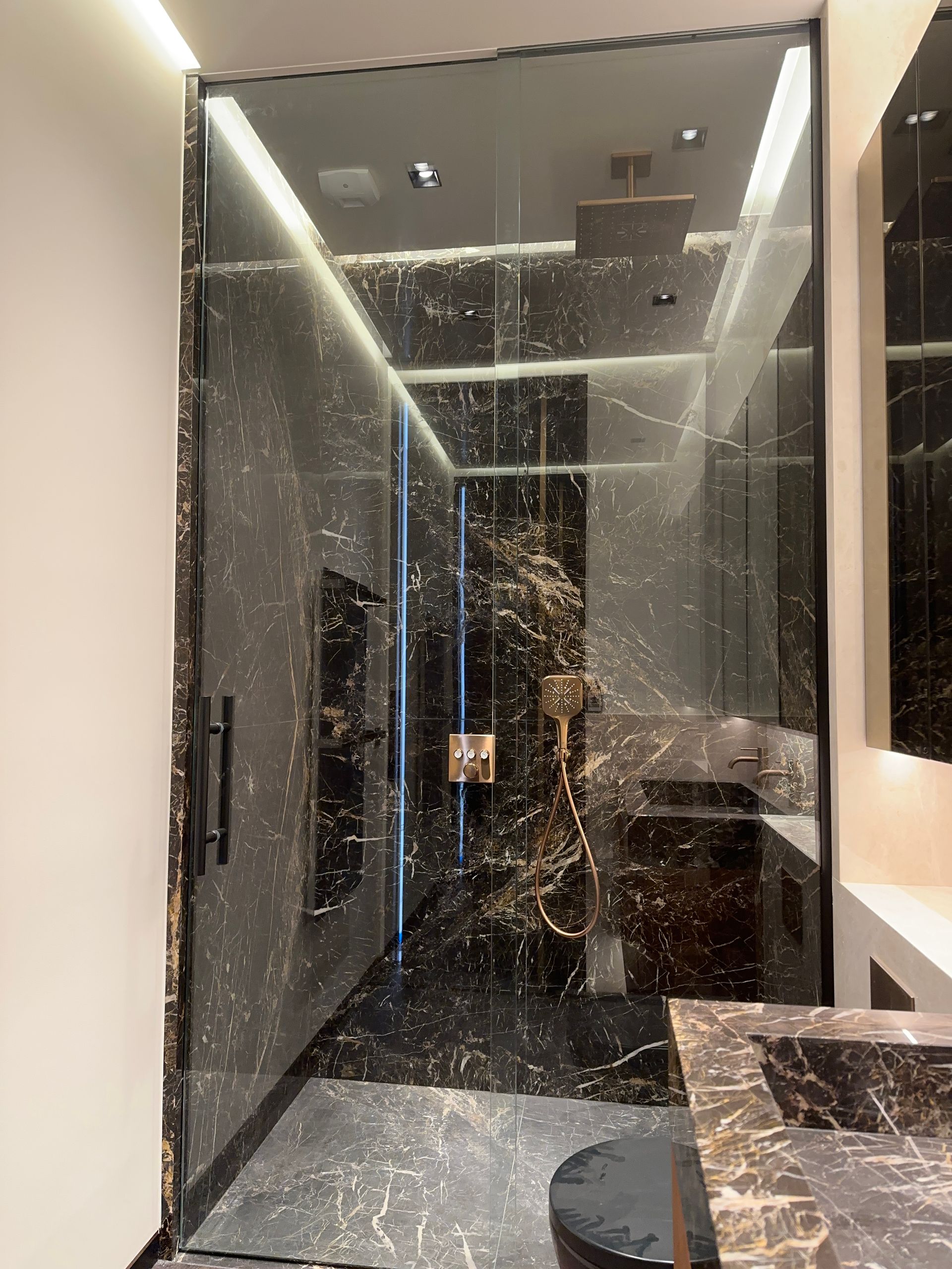 Douche en marbre de luxe avec porte vitrée et accessoires dorés.