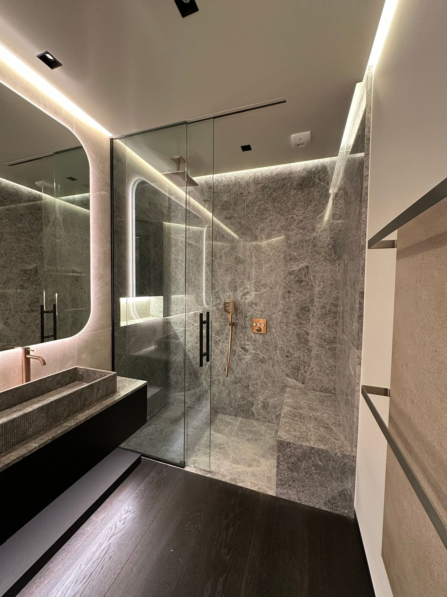 Salle de bain moderne avec murs en pierre grise, douche en verre et vanité noire.