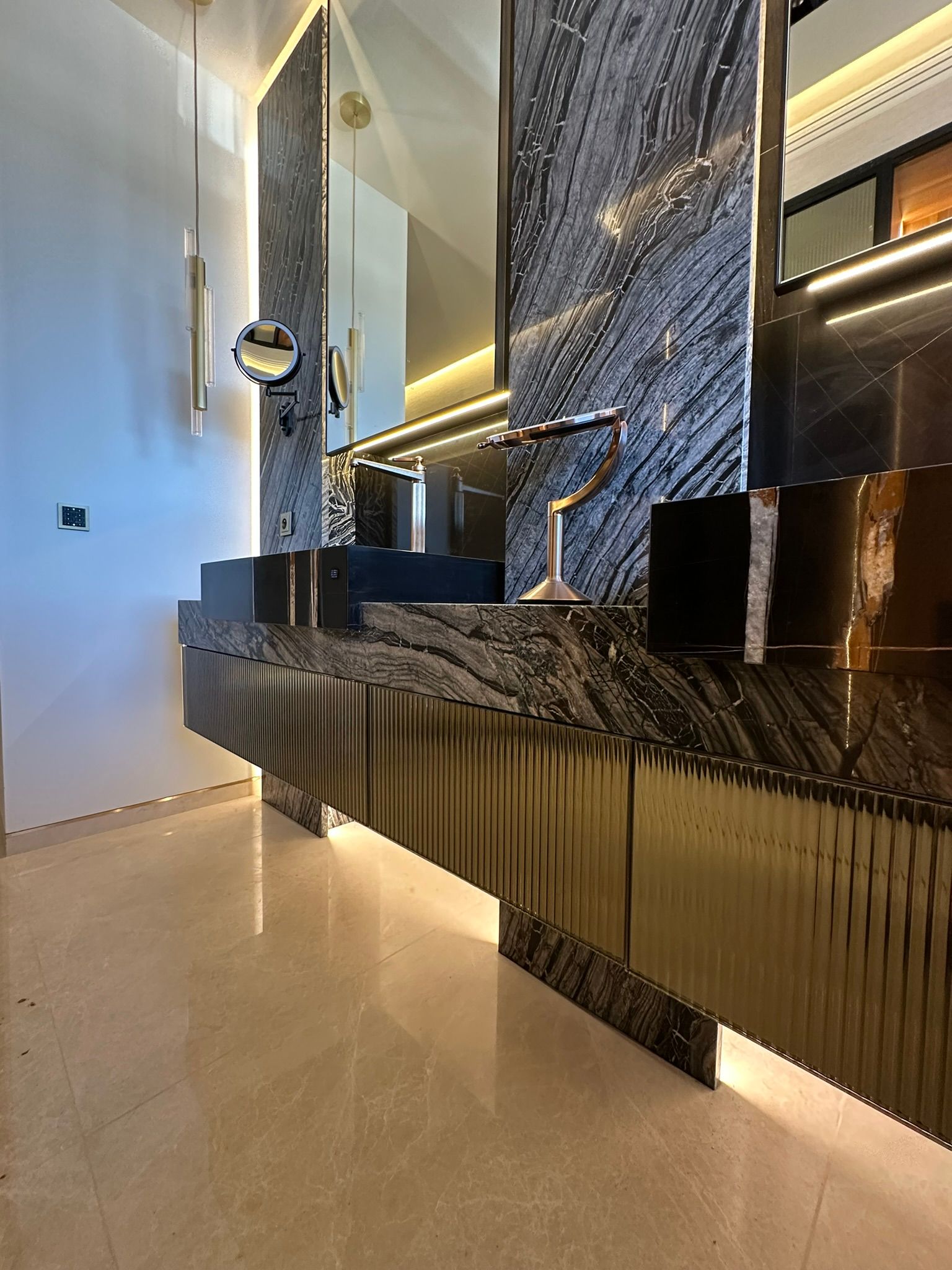 Luxueuse vanité de salle de bain noire et dorée avec surfaces texturées et luminaires modernes.