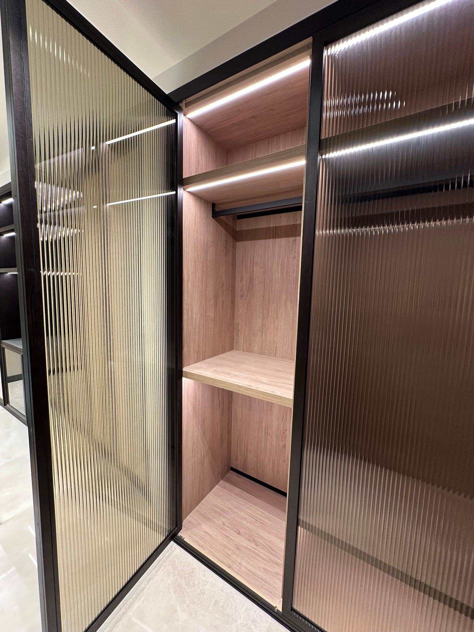 Placard avec portes en verre texturé, étagères et tringle à vêtements, avec éclairage intérieur.