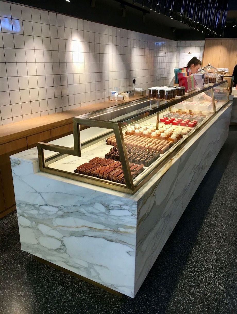 Une vitrine recouverte de marbre remplie de pâtisseries dans un magasin ; une personne se trouve derrière le comptoir.
