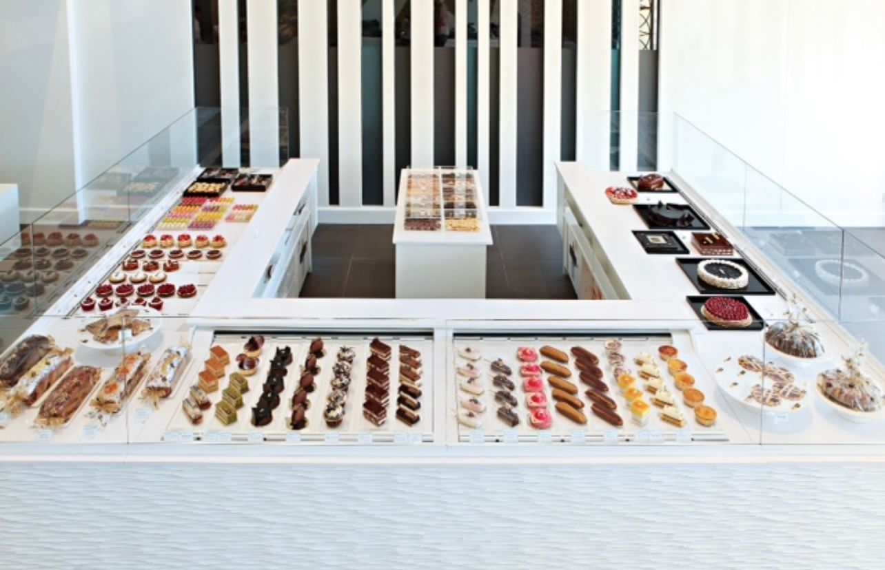 Une vitrine blanche avec un assortiment de pâtisseries et de desserts. Un mur rayé noir et blanc en toile de fond.
