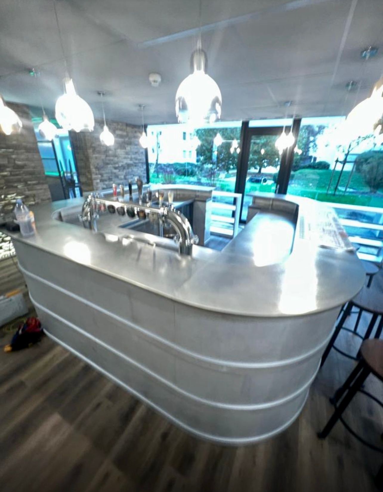 Bar avec surface et robinetterie en métal brillant. Suspensions, grande fenêtre et parquet.