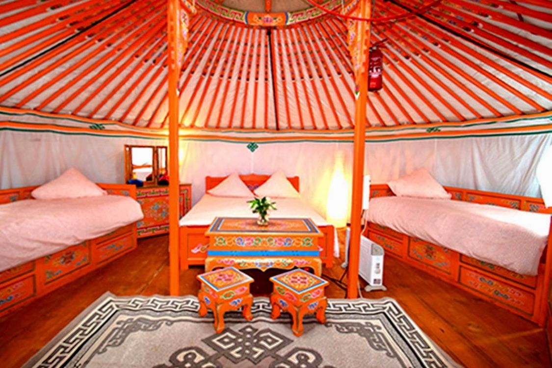 Intérieur d'une yourte orange : lits, tables et tapis, avec une pièce maîtresse florale.