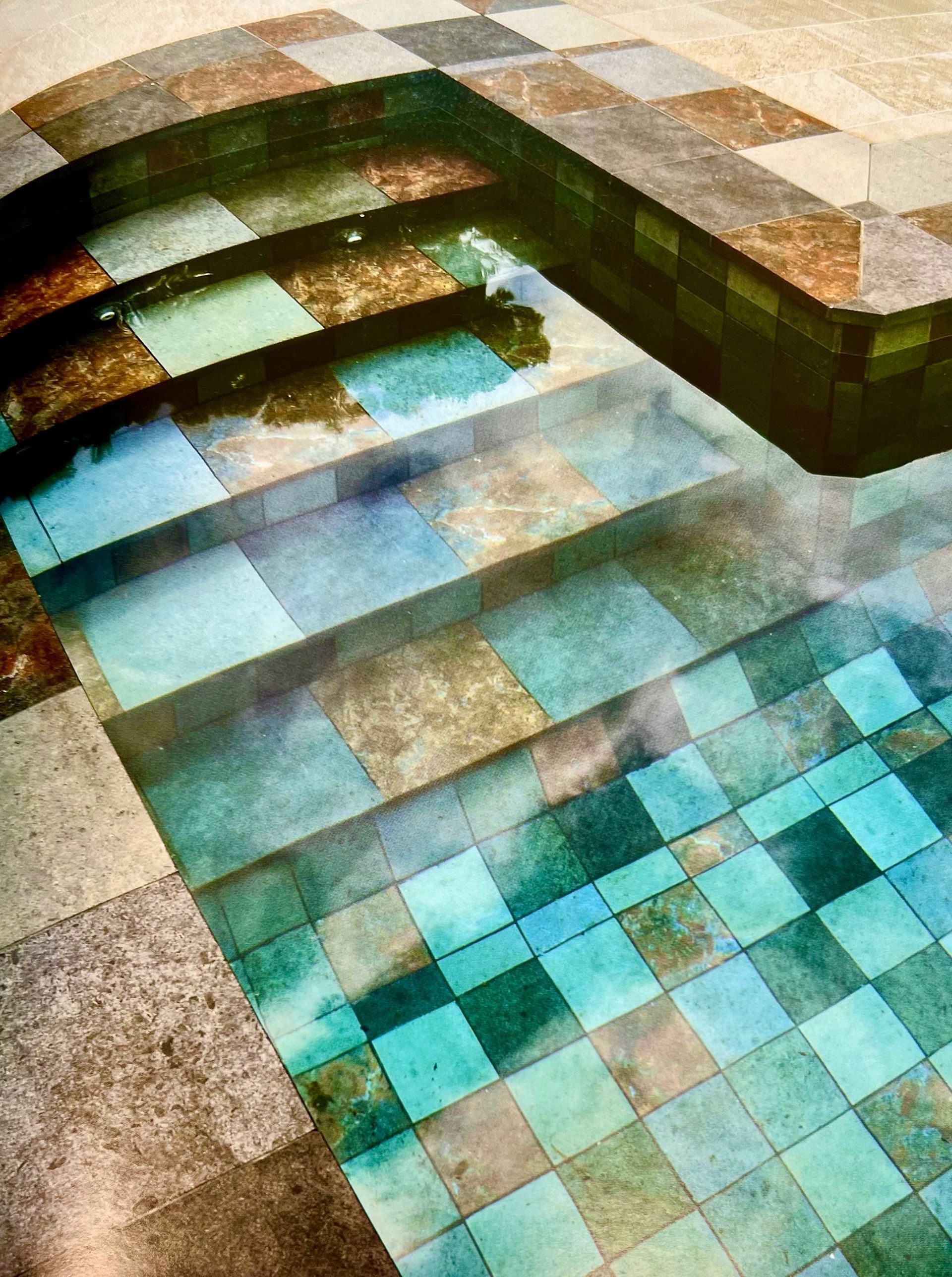 Piscine avec carrelage en damier, marches et eau reflétant différentes nuances de bleu et de vert.
