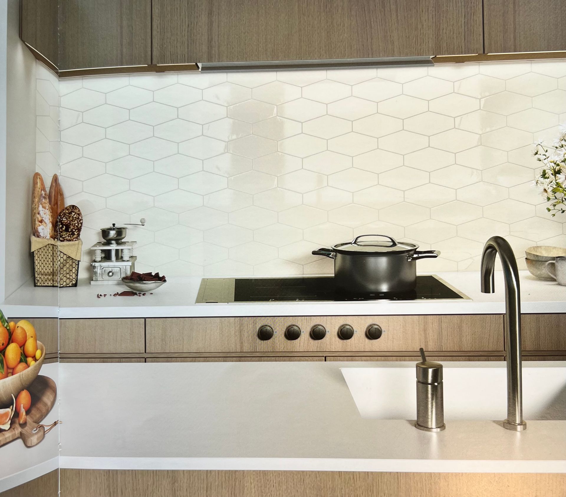 Cuisine moderne avec comptoir blanc, cuisinière, évier et dosseret en carreaux géométriques.