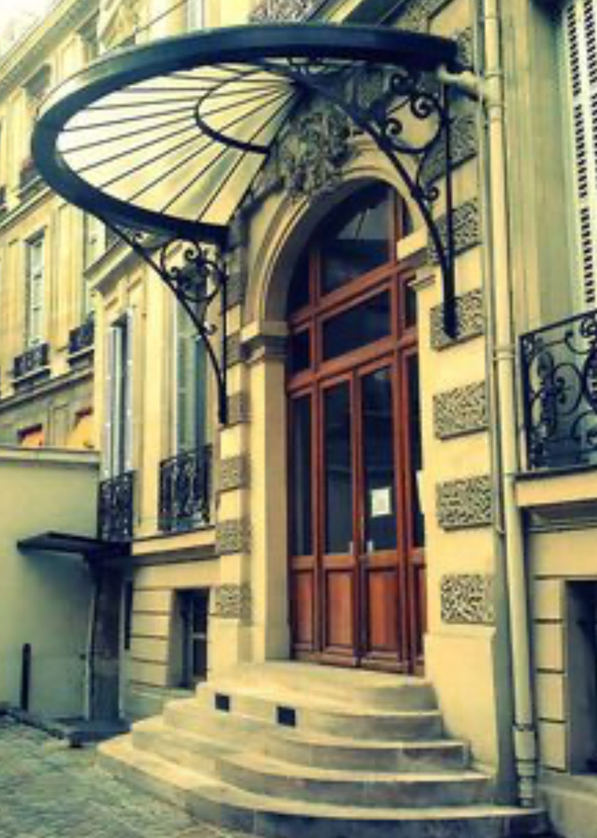 Entrée voûtée ornée avec auvent et portes en bois. Un escalier en pierre mène à l'entrée du bâtiment.