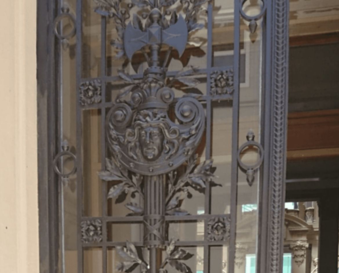 Porte en métal sombre et ornée avec des sculptures détaillées, notamment un visage, une hache et du feuillage.