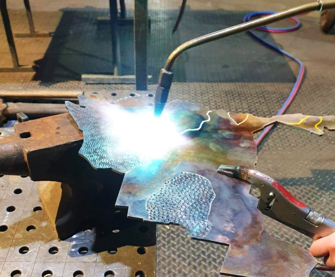 Une personne soudant du métal avec une flamme bleue et blanche brillante dans un atelier, sur une enclume.