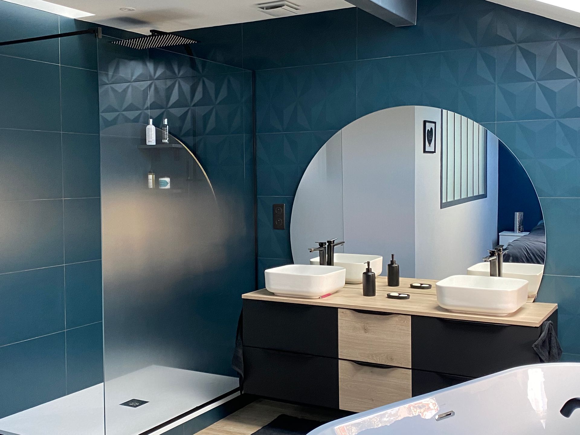 Salle de bain moderne avec murs en carrelage texturé bleu sarcelle, miroir circulaire, meuble-lavabo double et douche.
