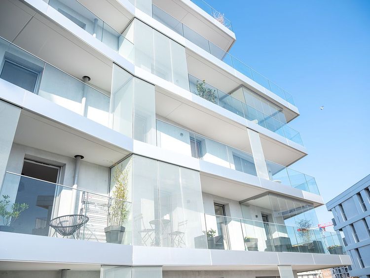 Immeuble d'appartements blanc moderne avec balcons en verre contre un ciel bleu clair.