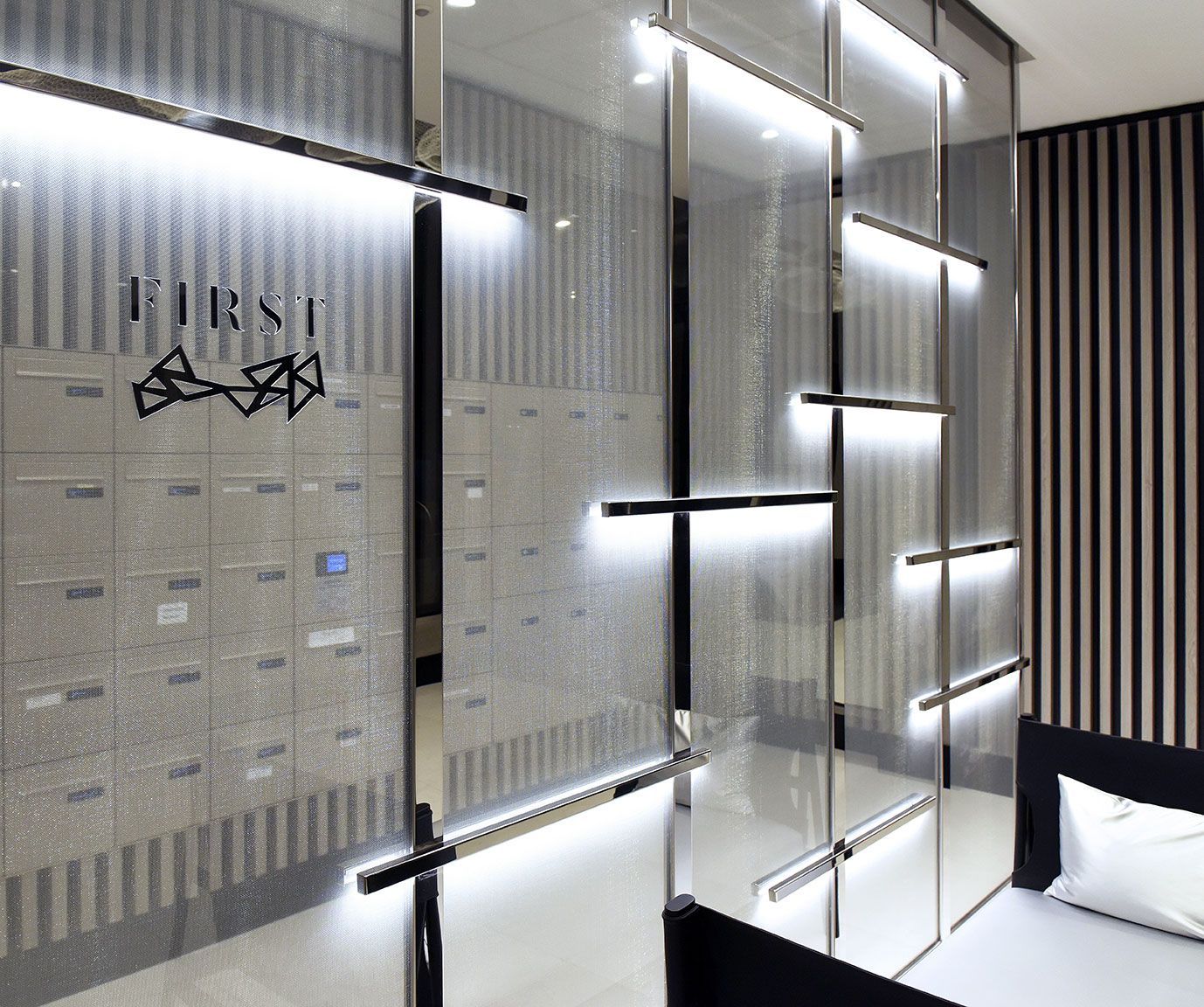 Hall d'entrée moderne avec boîtes aux lettres et cloison vitrée éclairée. Logo « FIRST » à gauche.