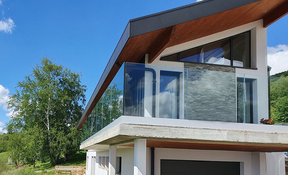 Maison moderne en construction avec murs en verre, boiseries et ciel bleu.