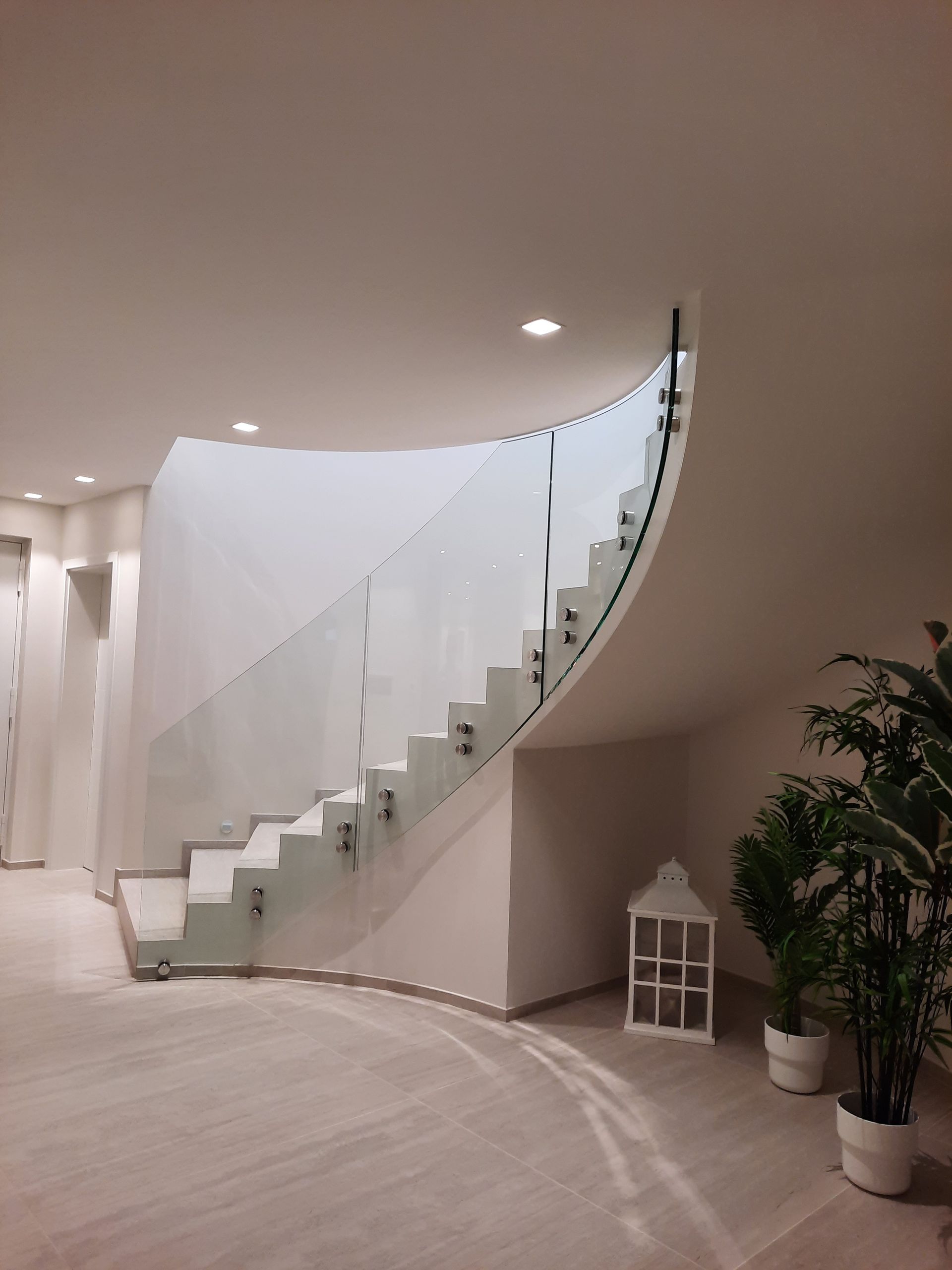 Escalier courbe moderne avec garde-corps en verre dans un espace blanc lumineux.
