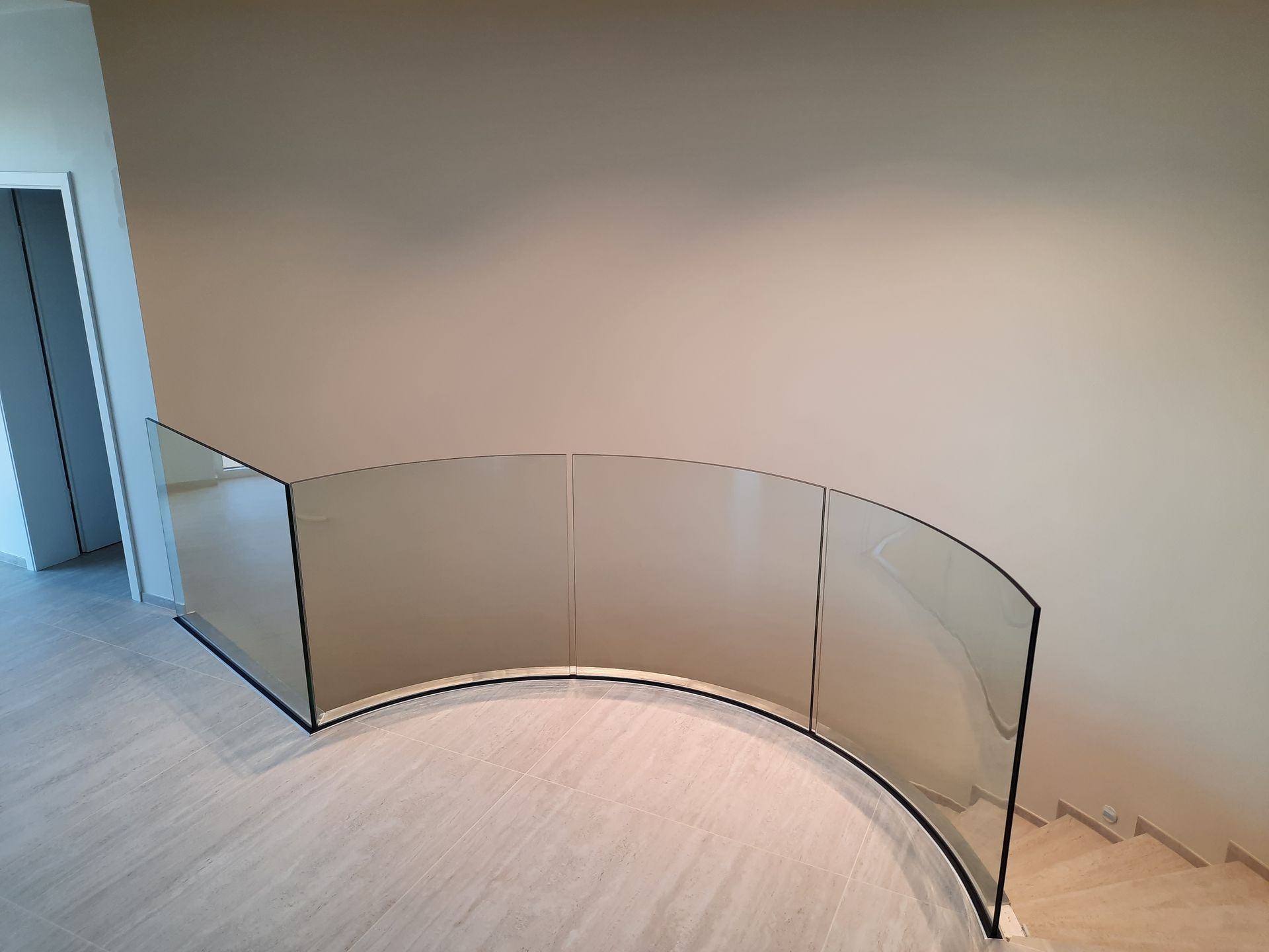 Garde-corps en verre courbé avec garniture noire le long d'un mur et d'un sol de couleur claire, près des escaliers.