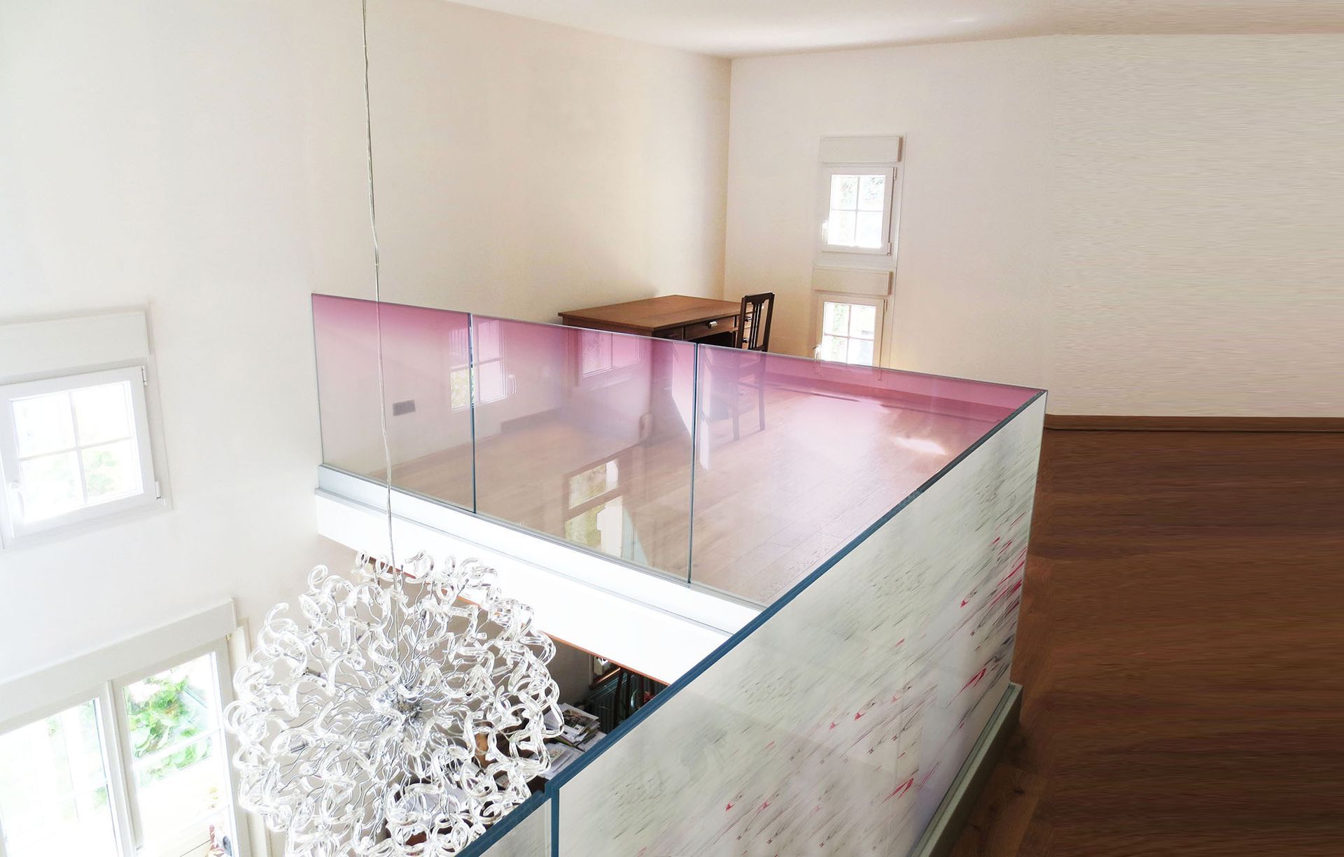 Niveau mezzanine avec garde-corps en verre et dégradé rose; plancher en bois et table à manger en arrière-plan.