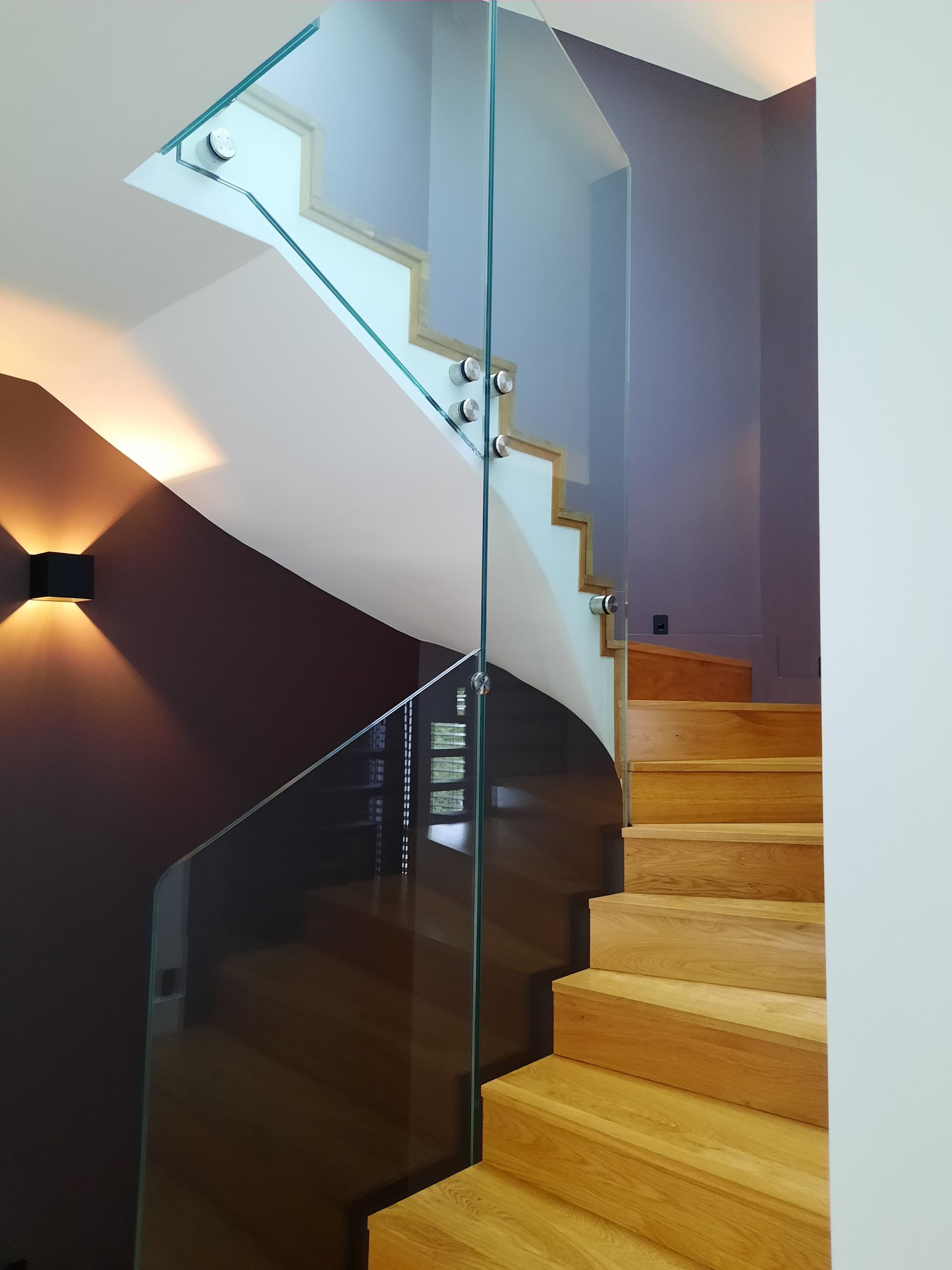 Escalier en bois avec rampe en verre, murs violets et blancs.
