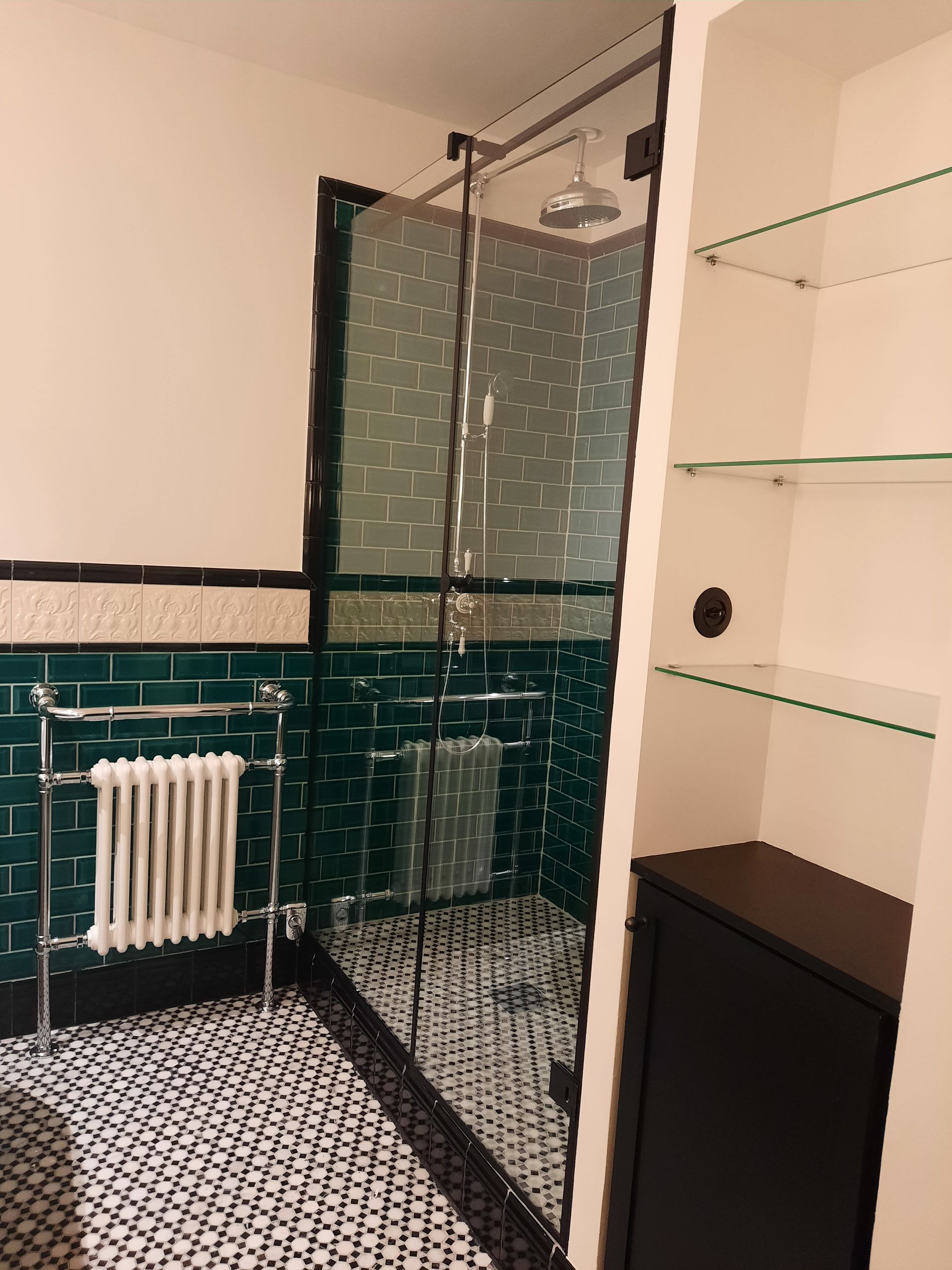 Salle de bain avec douche en verre, carrelage vert, radiateur et carrelage au sol noir et blanc.