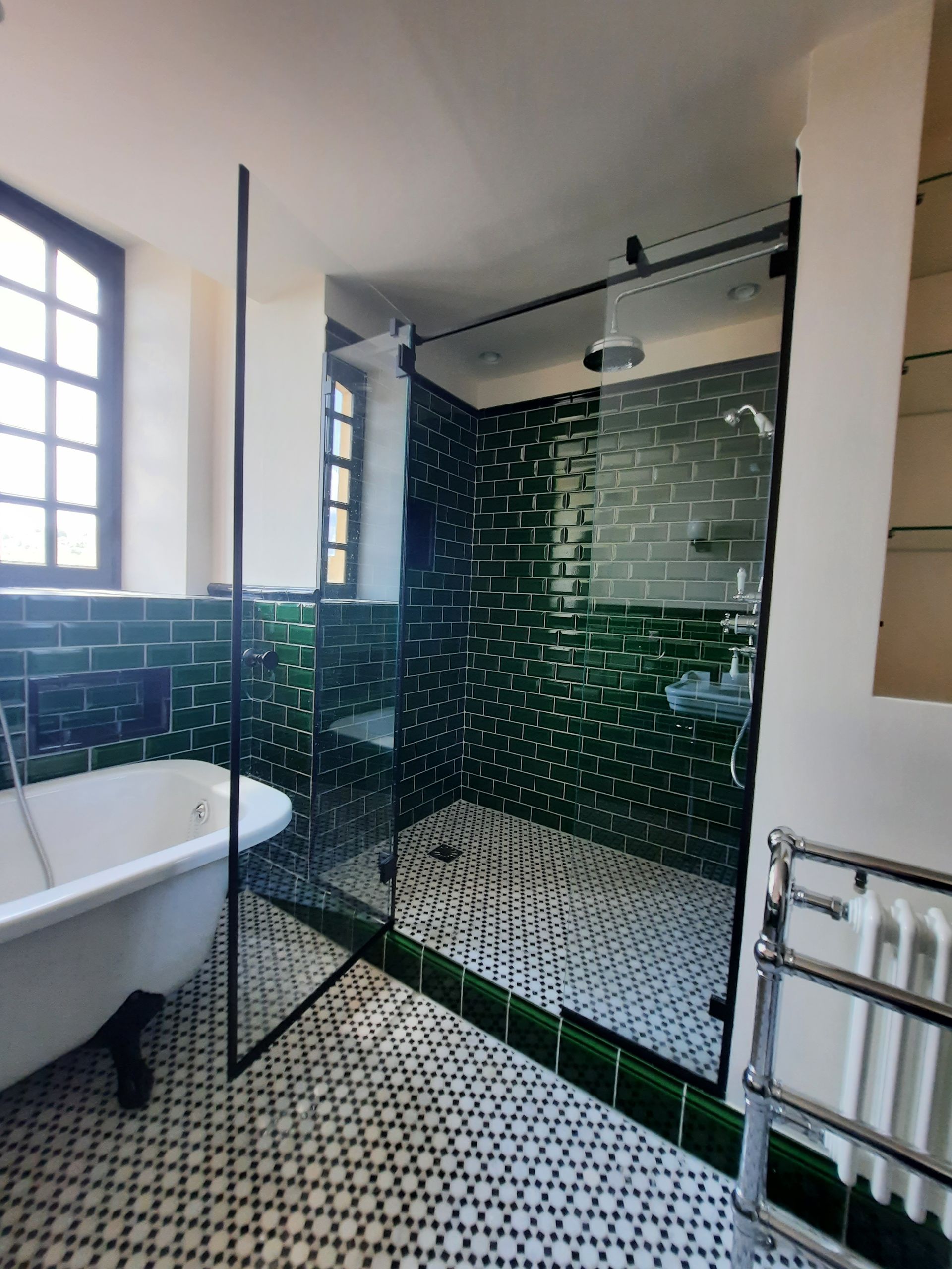 Salle de bain avec douche carrelée verte et baignoire sur pieds blanche. Sol carrelé noir et blanc.