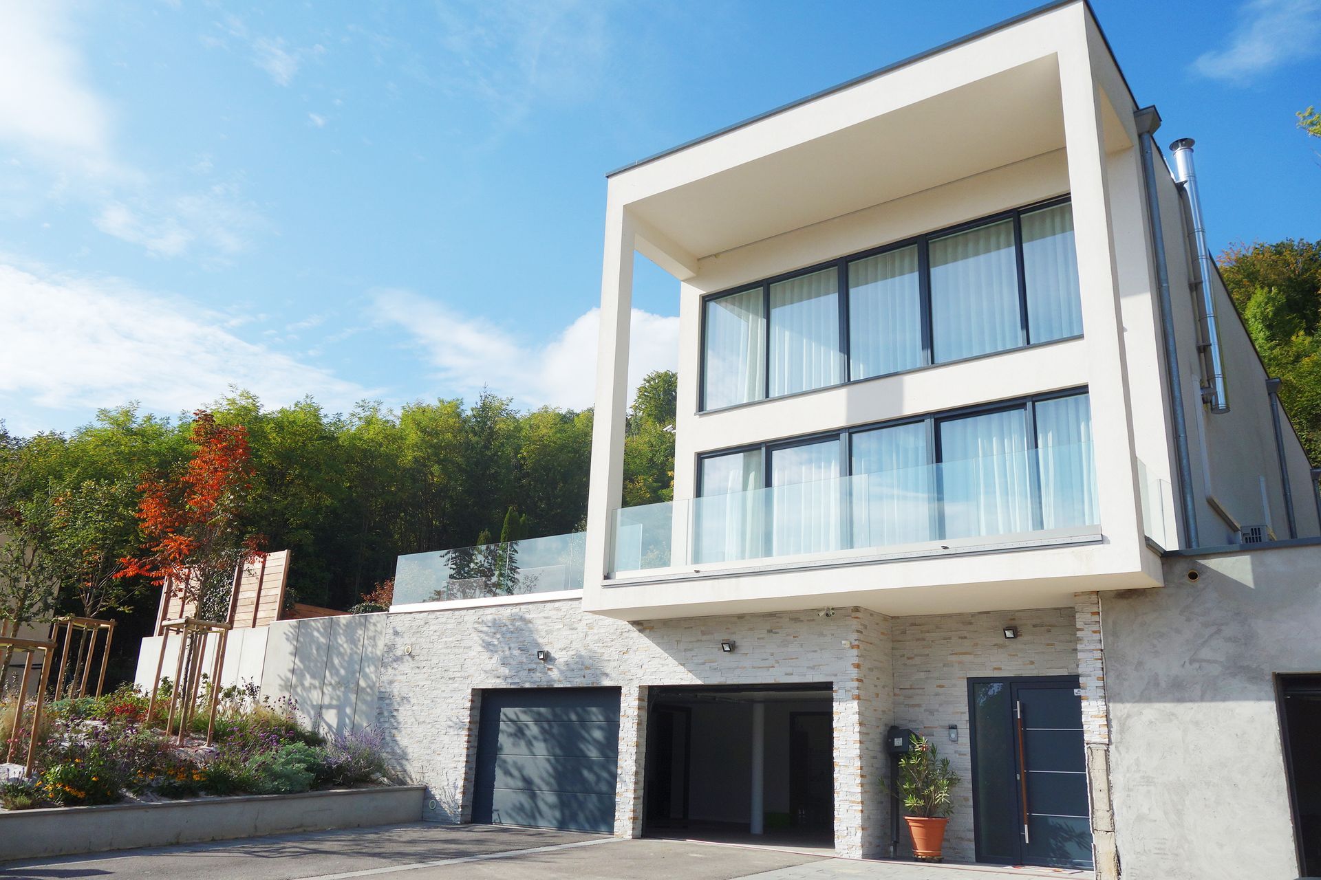 Maison moderne à deux étages avec baies vitrées, balcon et garage. Ciel bleu et façade en briques.